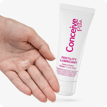 For Conceive Plus Max Combo - Fertility Lubricant Bundle, showing a close-up of 75ml fertility lubricant tube held near an open palm with a clear droplet of fertility-safe lubricant gel, highlighting product texture and gentle application for conception support.